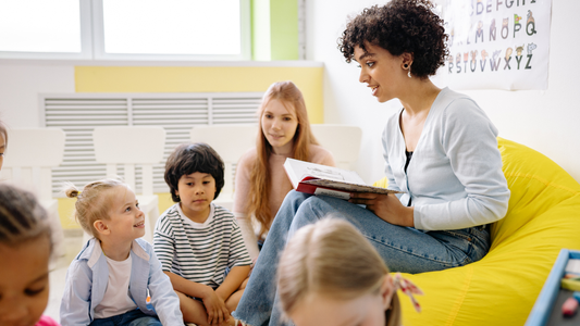 Woman sitting on a beanbag in a classroom reading a story to a group of young children