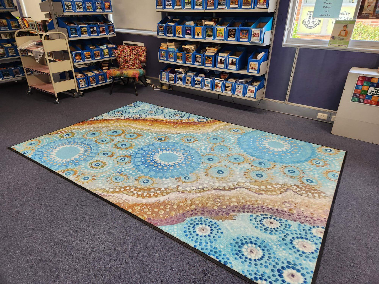River Country classroom rug, 2m x 3m, amazing blues and natural tones. Indigenous art, durable with non-slip and non-trip design. Shown in school library.